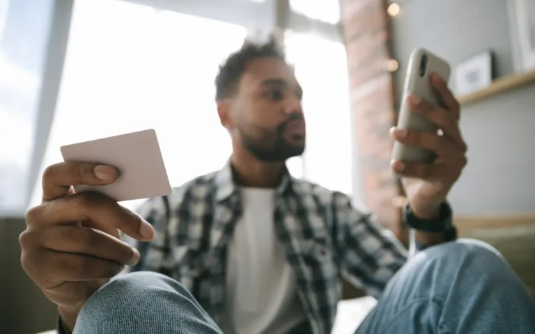 Homem em casa segurando o celular e um cartão sem identificação visível
