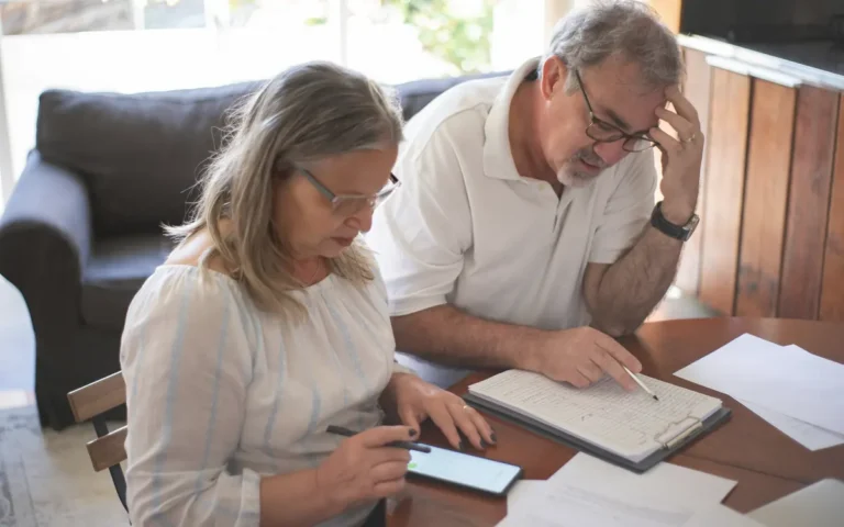 Casal de idosos analisando documentos e celular à mesa
