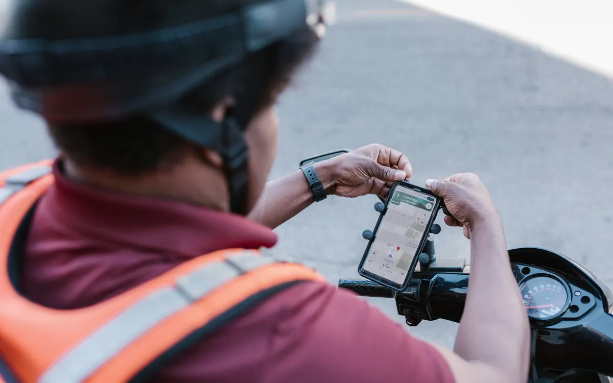 Entregador de aplicativo de capacete consultando o celular preso ao guidão da moto