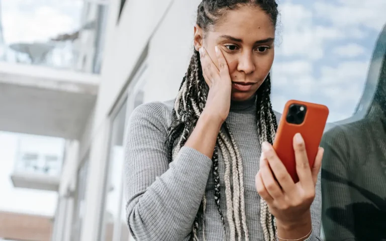 Mulher com expressão preocupada olhando para o celular na rua