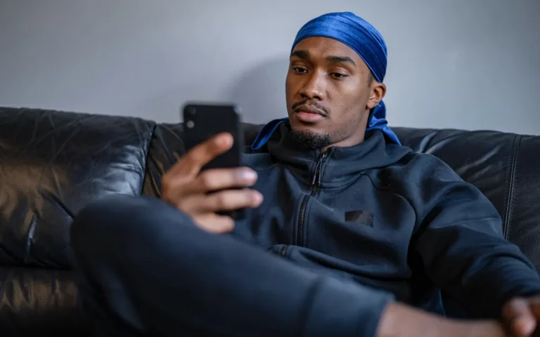 Homem sentado no sofá olhando a tela do celular