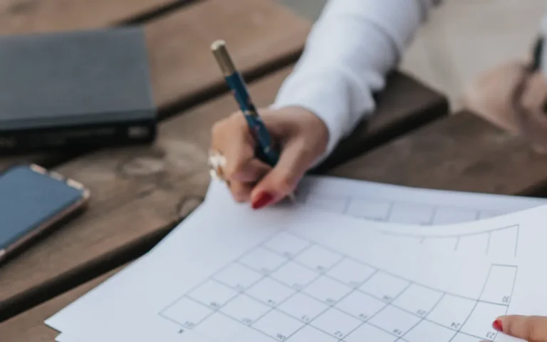 Pessoa anotando datas num calendário de papel sobre uma mesa